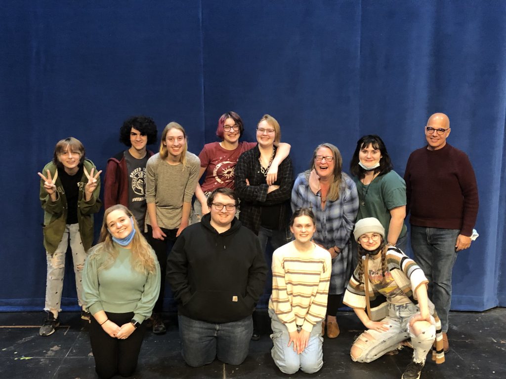 A photo of playwright Brenda Fager and the cast of high school students who performed her play, Chasing the Carpe Diem. Brenda is laughing, and the students have their arms around each other, and they are joined by Brenda's mentor Greg Fletcher.