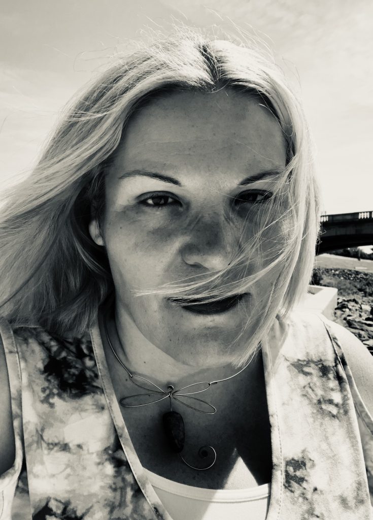 Black and white headshot of Kristin Ivey who is outside with wind blowing her hair across her face.