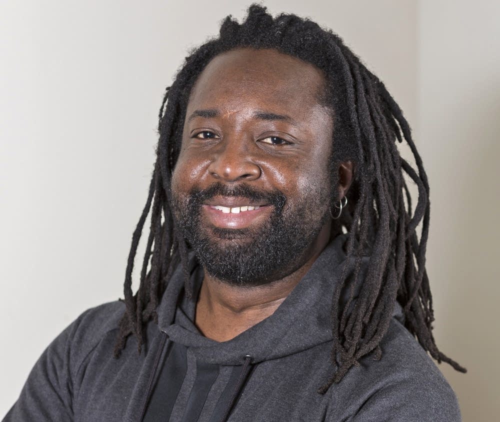 Headshot photo of writer Marlon James smiling and wearing a dark gray hooded sweatshirt.