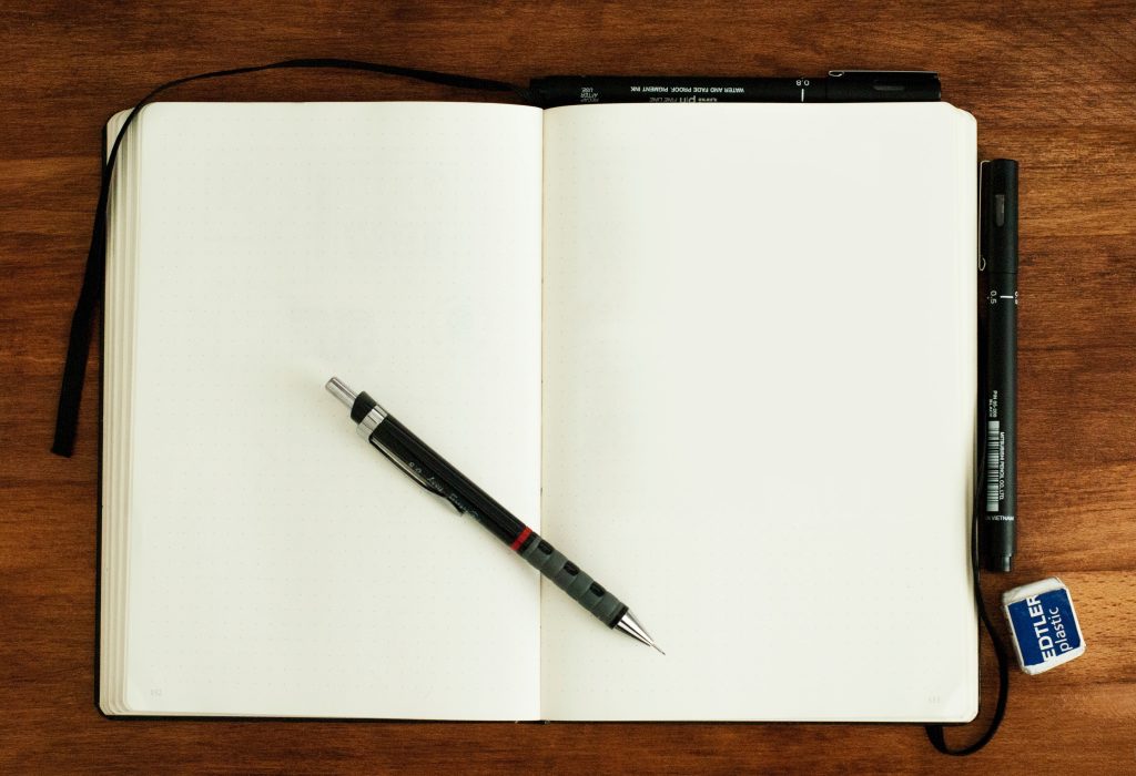 Photo of a notebook open to a blank page with a pen across its center